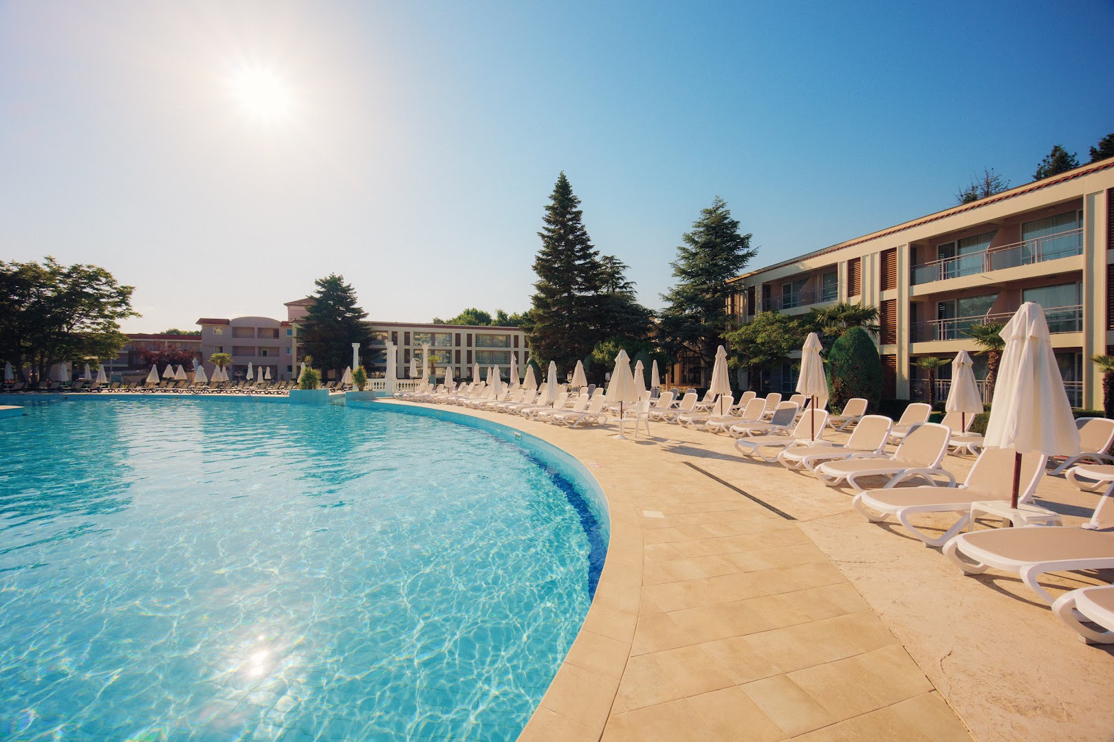 DIT Evrika Beach Club Hotel baseina mala ar rindu sauļošanās krēsliem un saulessargiem — gaiša, saulaina diena pie ūdens