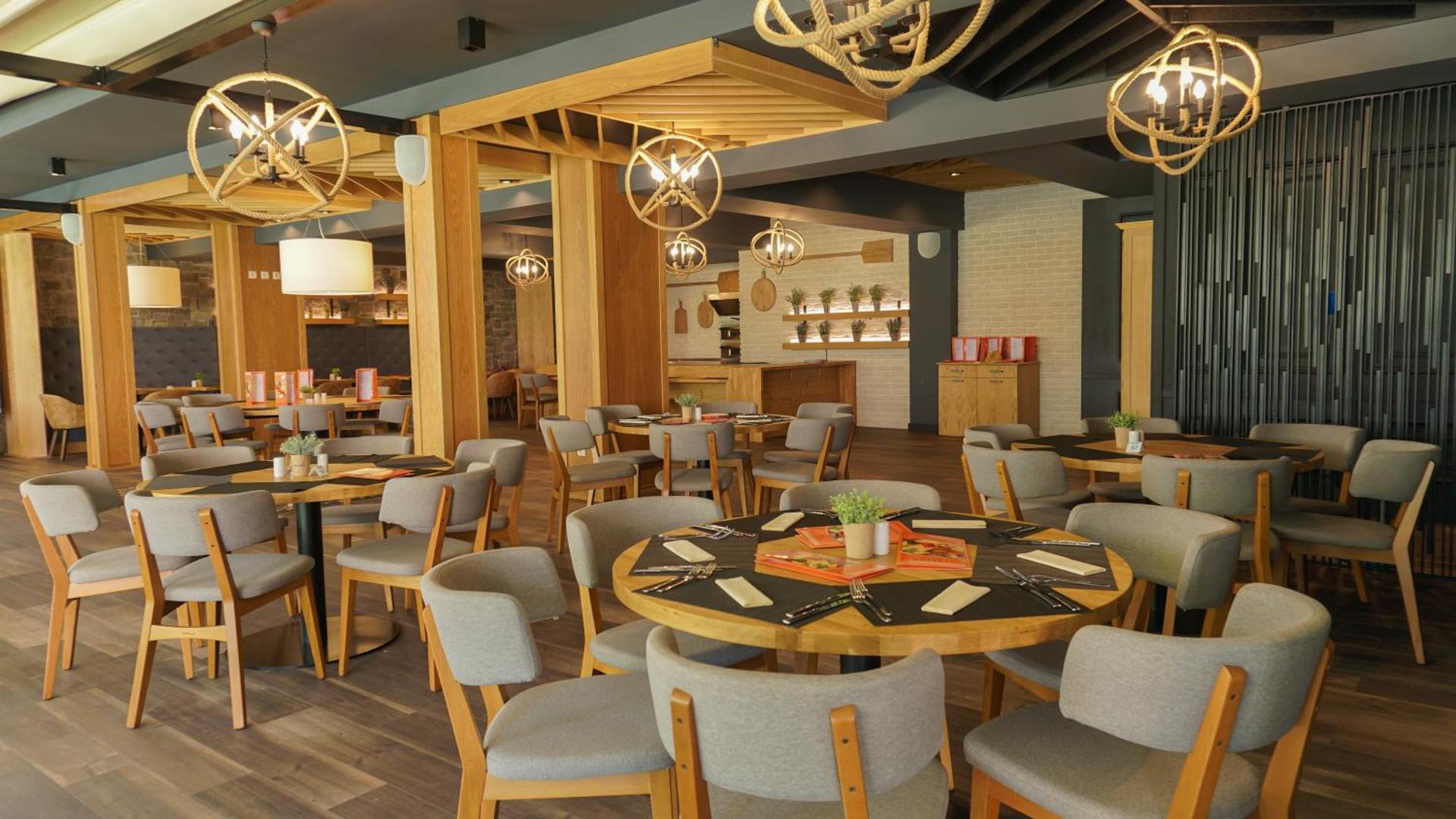 DIT Evrika Beach Club Hotel tematiskais restorāns ar koka interjeru, apaļiem galdiem un oriģināliem gaismas ķermeņiem mājīgai atmosfērai