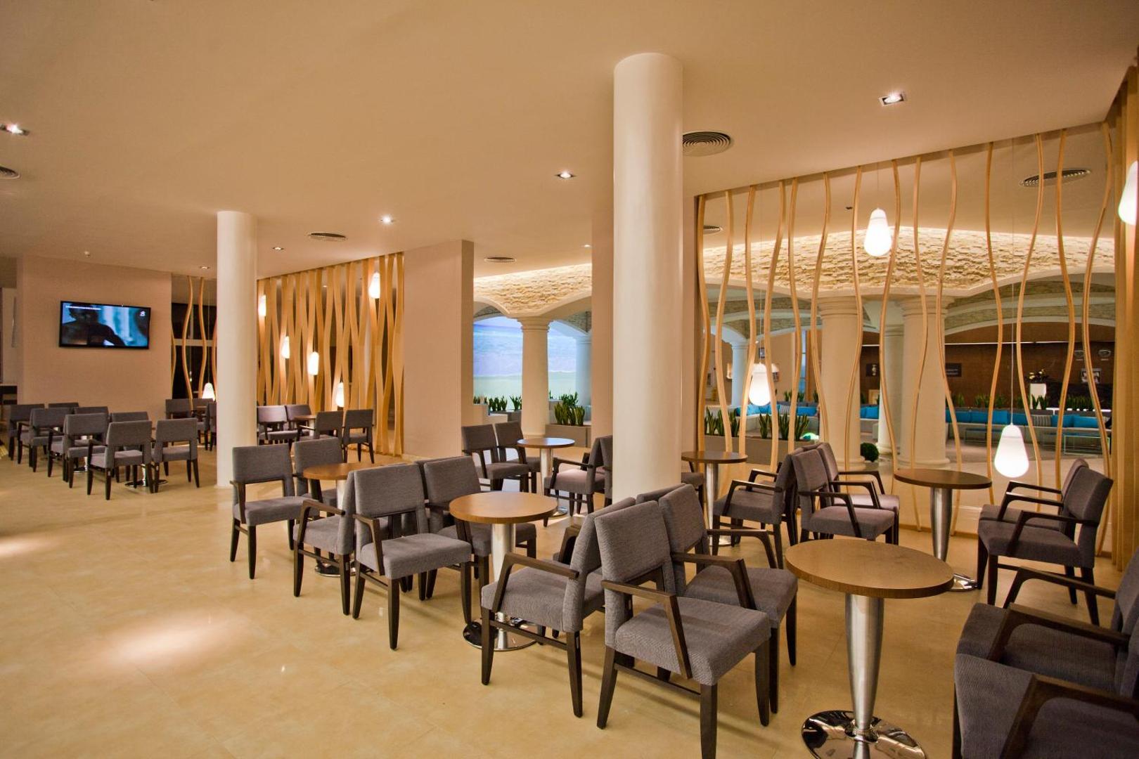 DIT Evrika Beach Club Hotel bāra un atpūtas telpa ar pelēkiem krēsliem, apaļiem galdiem un dekoratīvām koka starpsienām