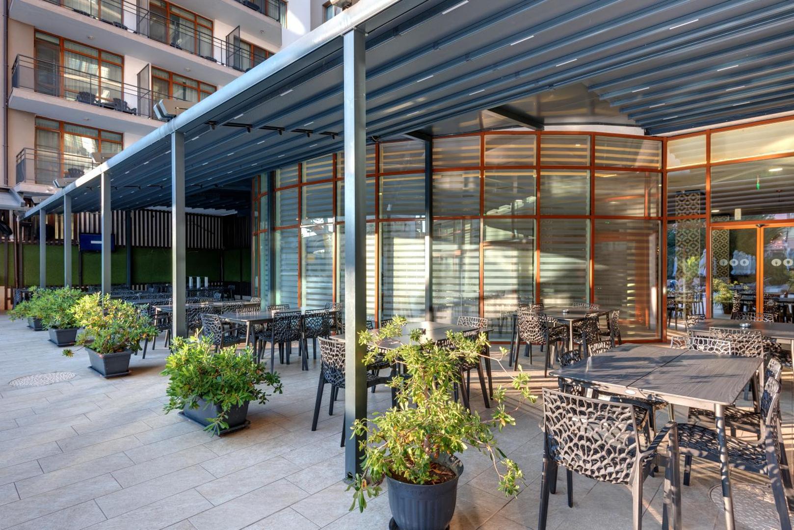 Best Western Plus Premium Inn viesnīcas āra terase ar moderniem galdiem un krēsliem zem nojumes, ko ieskauj dekoratīvi zaļumi