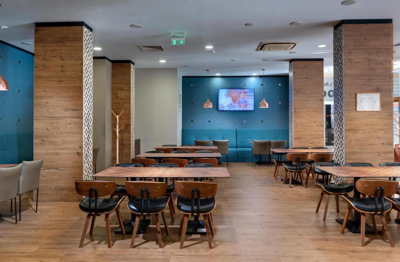 Best Western Plus Premium Inn restorāna iekštelpas ar koka apdari, modernām mēbelēm un zilu akcenta sienu ar televizoru
