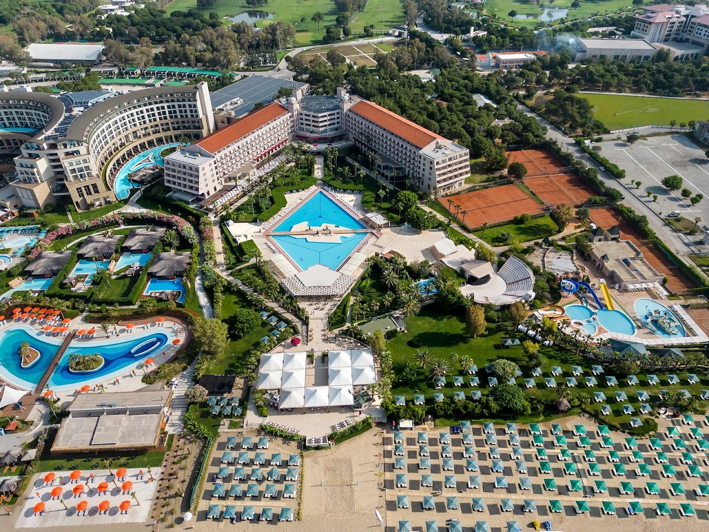 Kaya Belek kūrorta centrālā daļa ar romba formas baseinu, tenisa kortiem un bērnu ūdens atrakciju parku zaļā dārzā