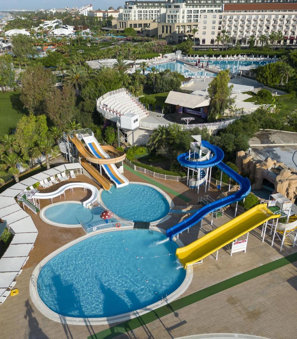 Kaya Belek akvaparks ar krāsainiem ūdens slidkalniņiem un bērnu baseiniem, fonā redzama viesnīcas teritorija un amfiteātris