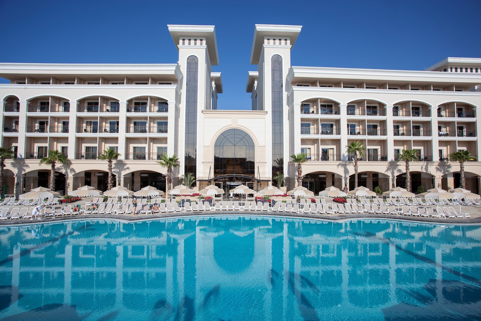 Dobedan Exclusive Hotel & Spa āra baseins dienas laikā ar sauļošanās krēsliem un saulessargiem pie viesnīcas fasādes