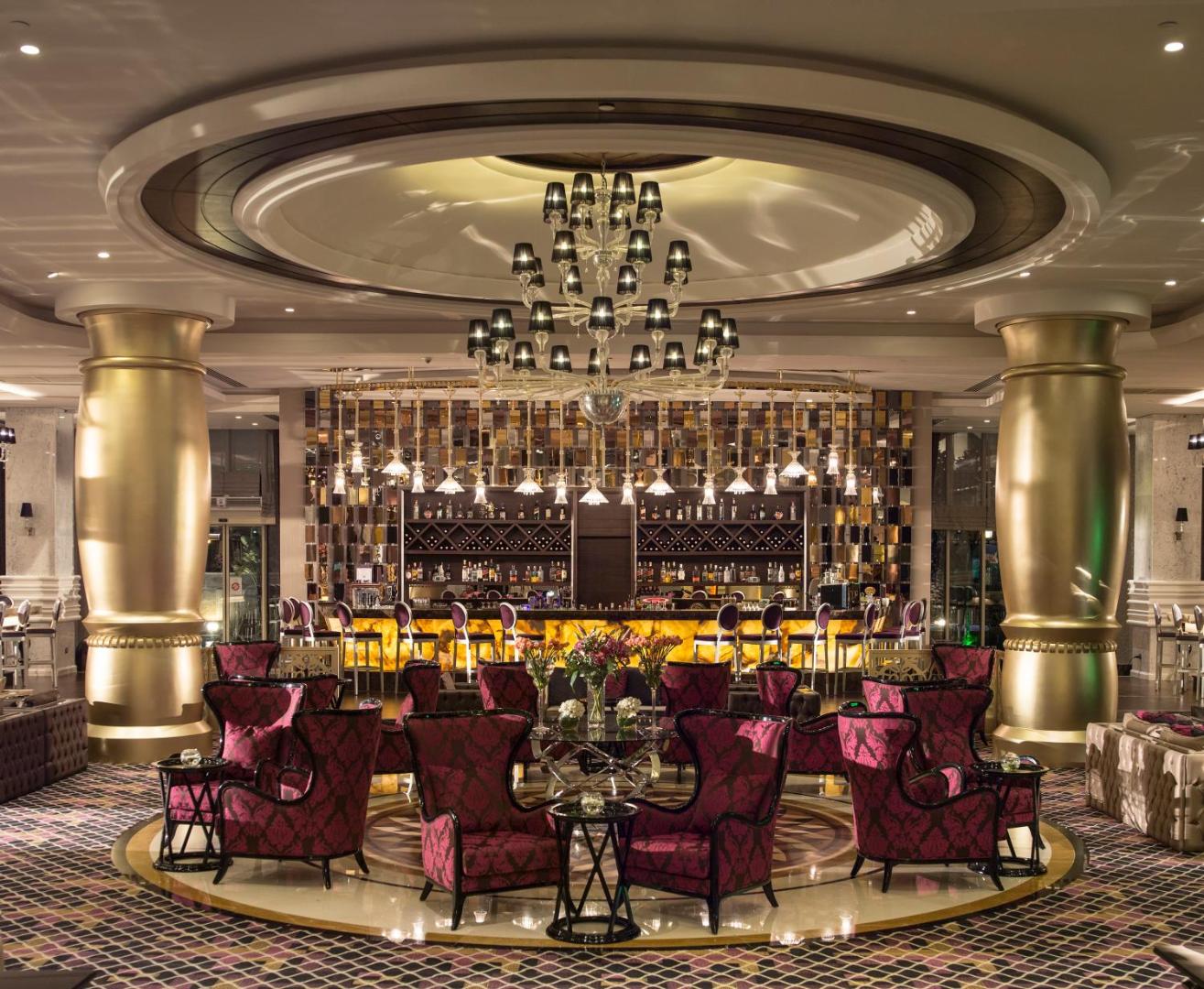 Dobedan Exclusive Hotel & Spa stilīgais lobby bārs ar modernu apgaismojumu, zelta kolonnām un violetiem atpūtas krēsliem vakara atmosfērā