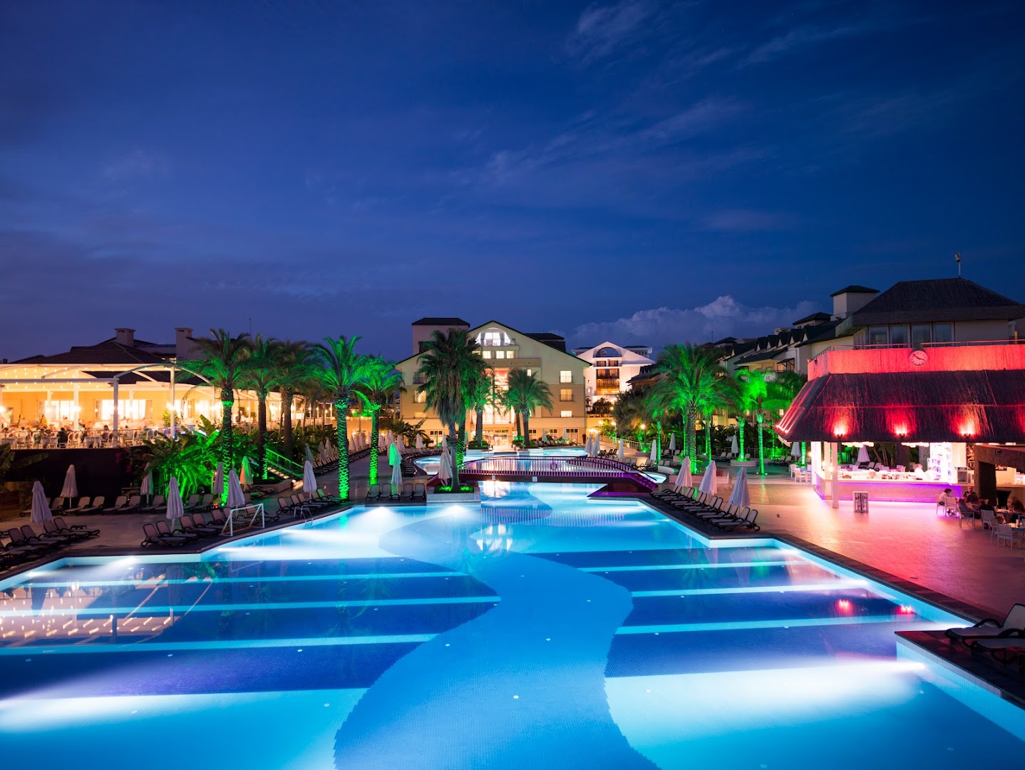 Dobedan Exclusive Hotel & Spa izgaismots baseins un bārs nakts noskaņās ar palmām un restorāna terasi fonā