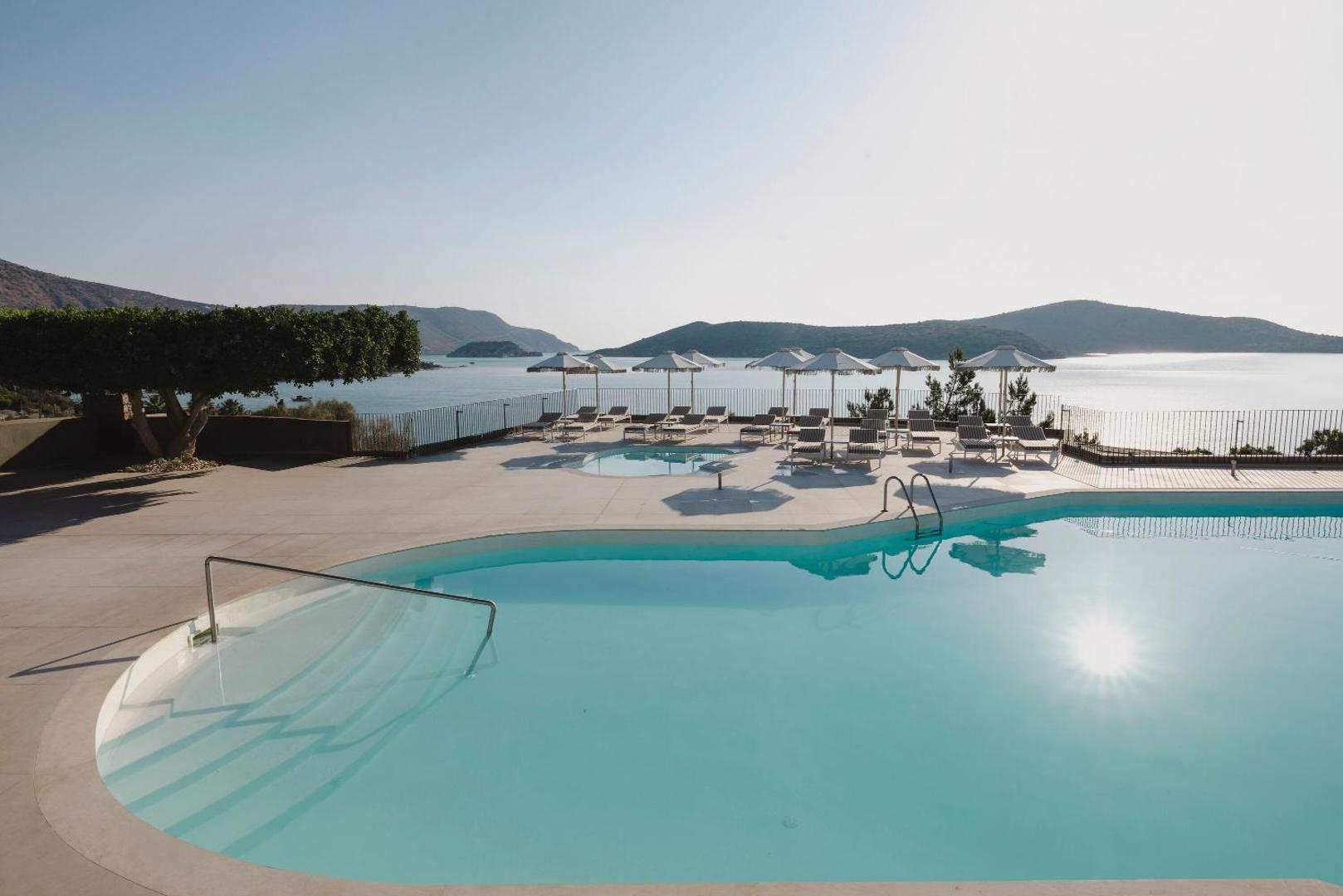 Domes Aulus Elounda Resort baseina zona ar saulessargiem un skatu uz jūru un kalnaino piekrasti