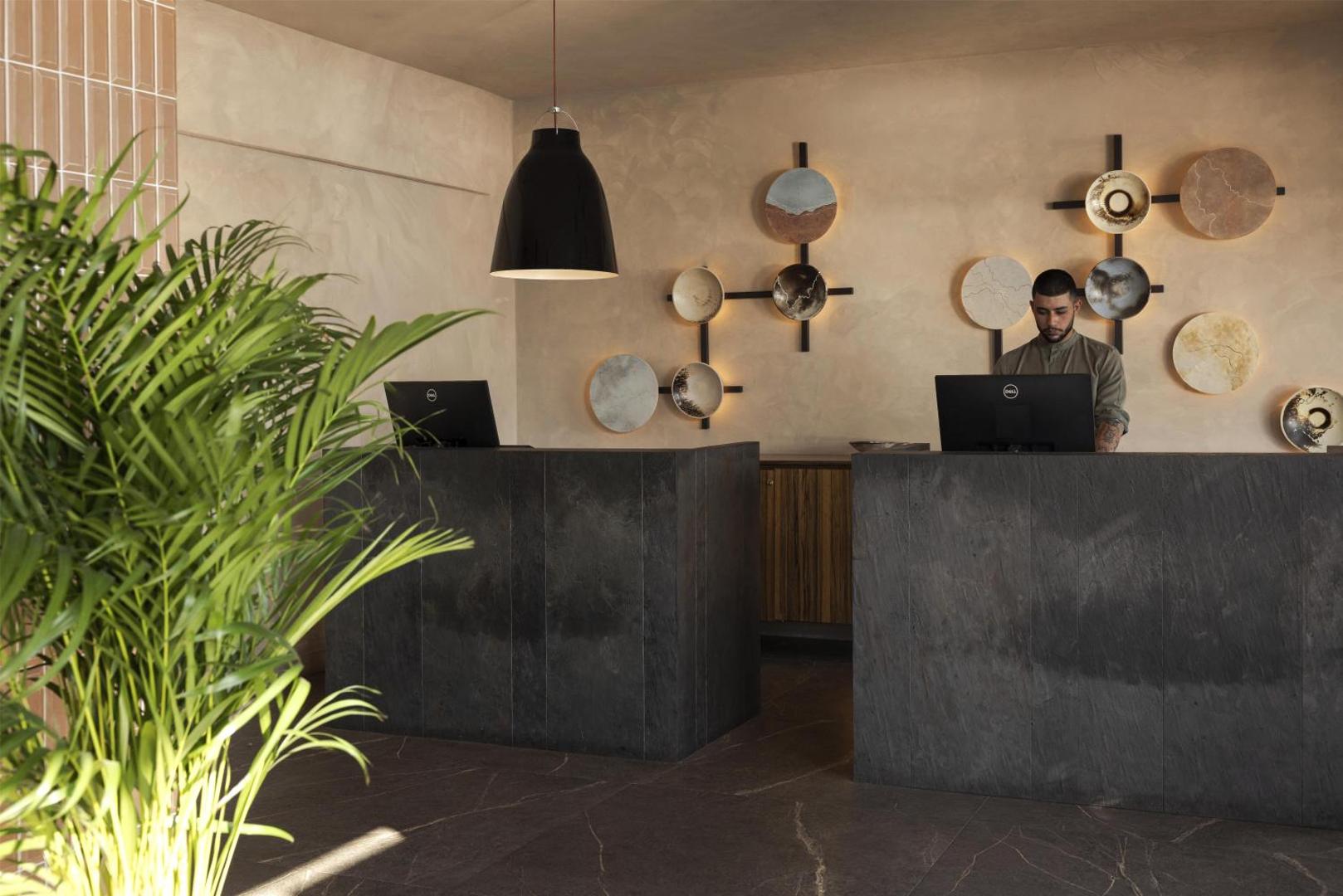 Domes Aulus Elounda Resort viesnīcas recepcijas zona ar tumša akmens letēm un māksliniecisku sienas dekoru Krētā