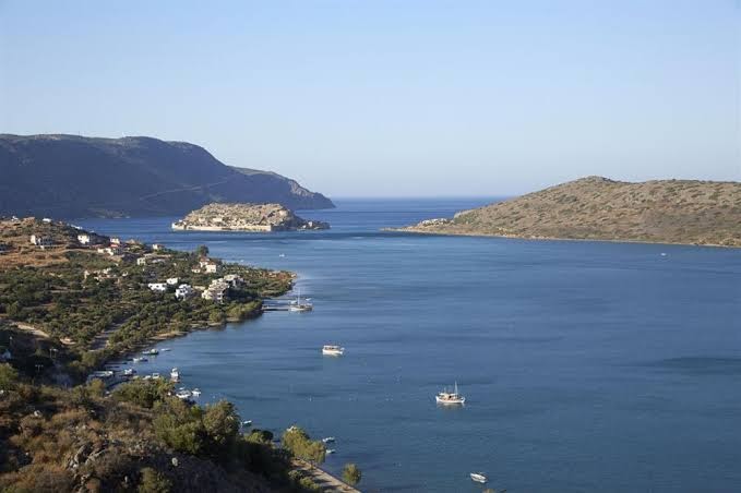 Domes Aulus Elounda skats no augšas uz Mirabello līci un Spinalongas salu Krētā — piekrastes ainava ar zilām laivām