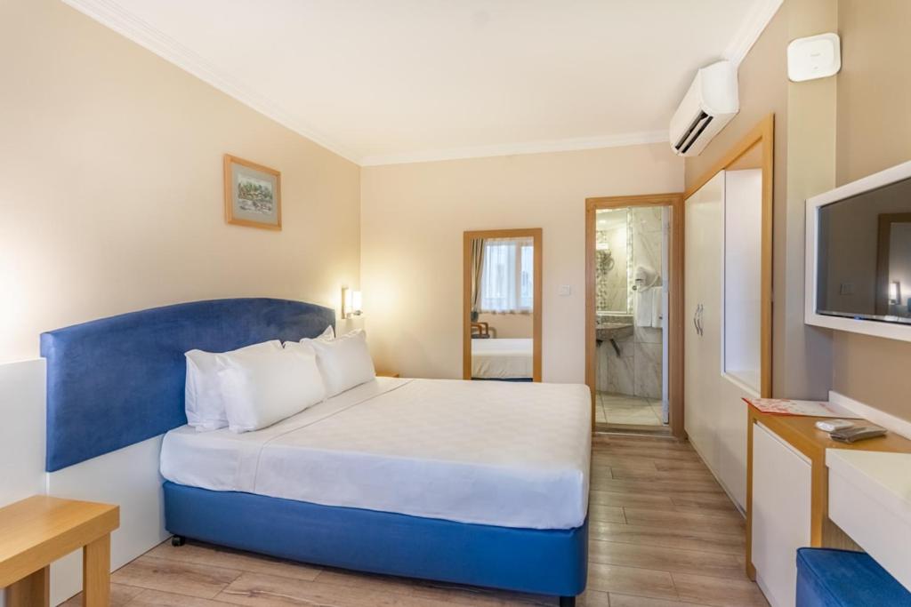 L'ancora Beach Hotel gaišs numurs ar divguļamo gultu, zilu galvgali un koka grīdu — redzama ieeja vannas istabā un spogulis
