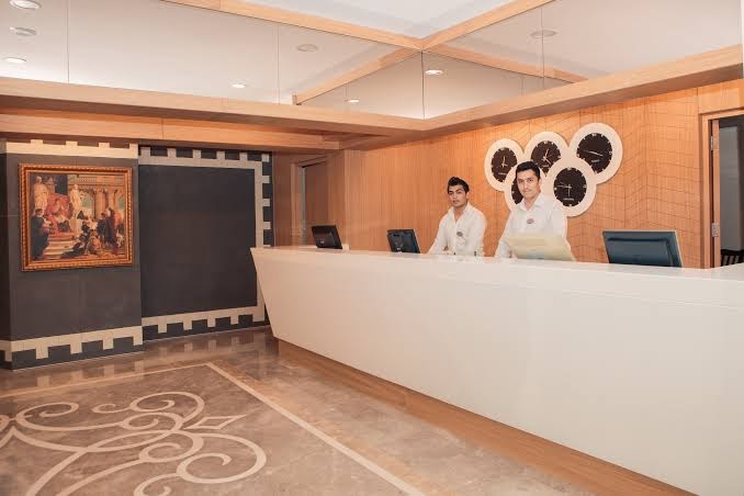 L'ancora Beach Hotel modernā recepcijas lete ar viesmīlīgu personālu un stilīgu sienas dekoru viesnīcas foajē.