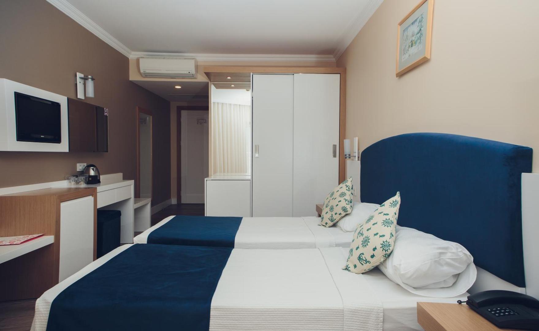 L'ancora Beach Hotel numurs ar divām atsevišķām gultām, ziliem dekoratīviem spilveniem un baltu skapi — mājīgs iekārtojums atpūtai