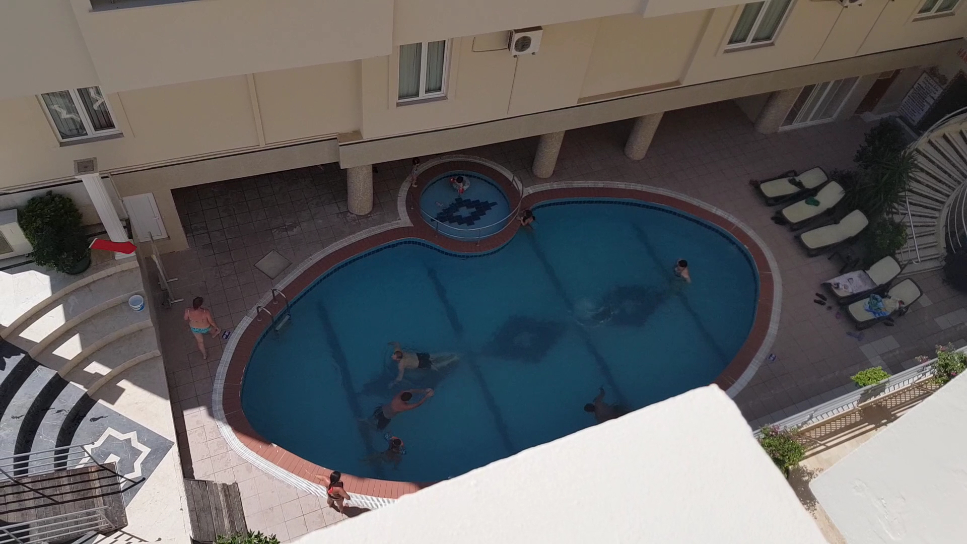Skats no augšas uz L'ancora Beach Hotel ovālo baseinu un bērnu baseinu — apkārt izvietoti sauļošanās krēsli un viesnīcas korpusi