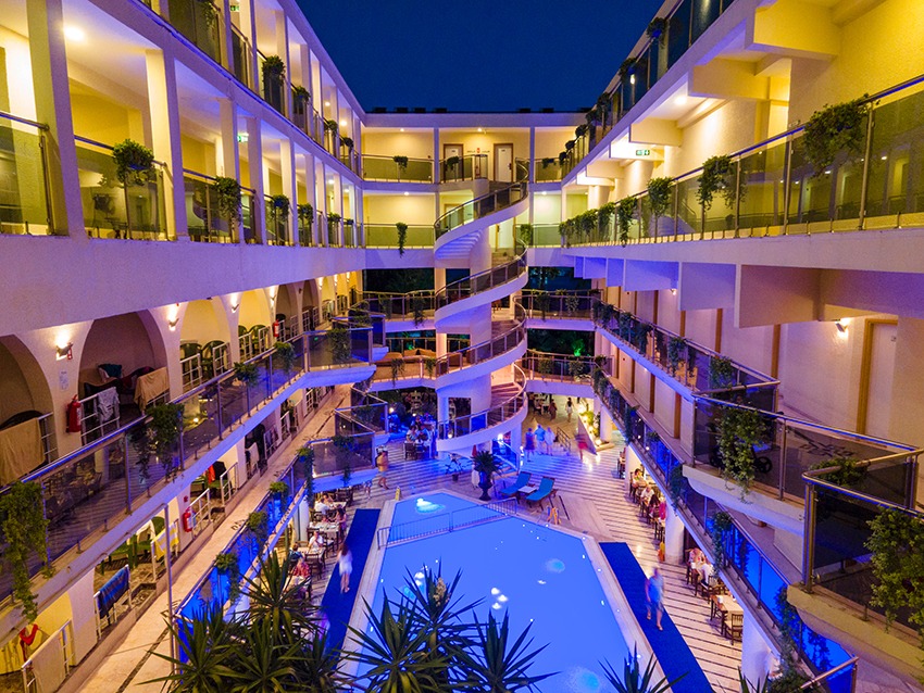 L'ancora Beach Hotel iekšpagalms vakarā ar izgaismotu baseinu, spirālveida kāpnēm un restorāna zonu zem klajas debess