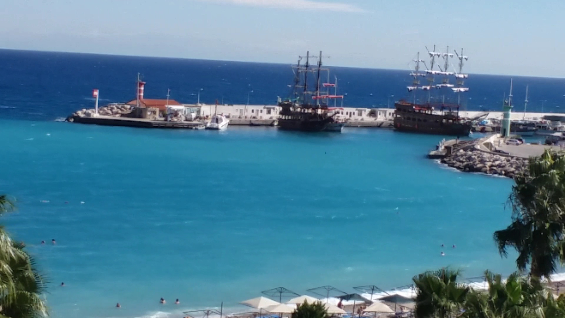 Skats uz Vidusjūras piekrasti un Kemeras ostu ar pirātu kuģiem — dzidrs ūdens un pludmales zona pie L'ancora Beach Hotel