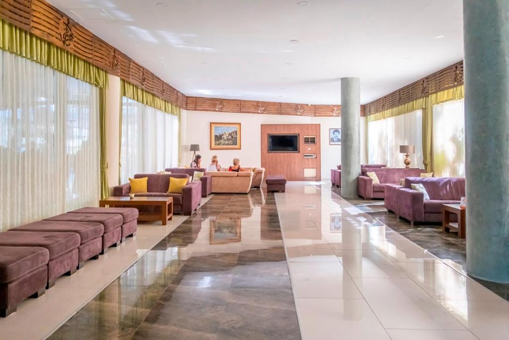 L'ancora Beach Hotel plašā lobby atpūtas zona ar mīkstiem dīvāniem, lieliem logiem un gaišu flīžu grīdu Kemeras kūrortā.