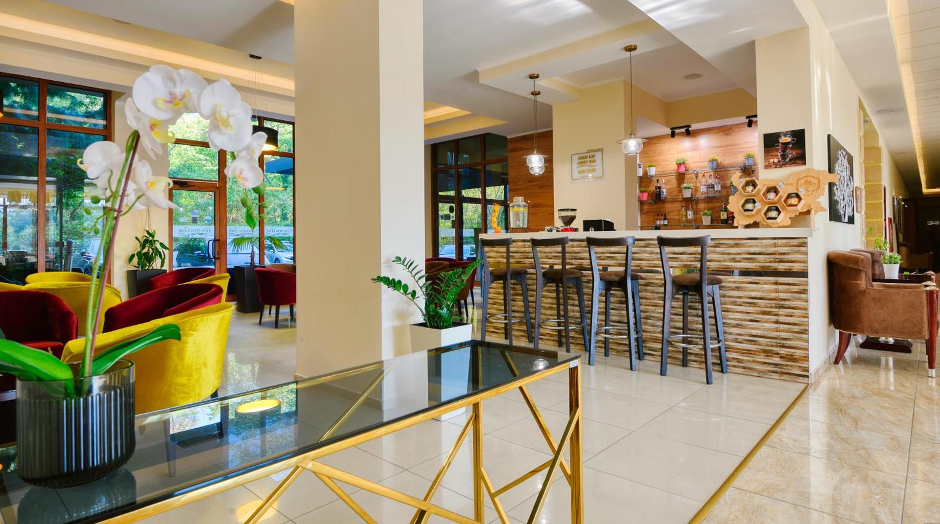 Golden Line lobby bārs ar modernu leti, augstiem krēsliem un krāsainu atpūtas zonu pie lieliem logiem ar skatu uz zaļumiem