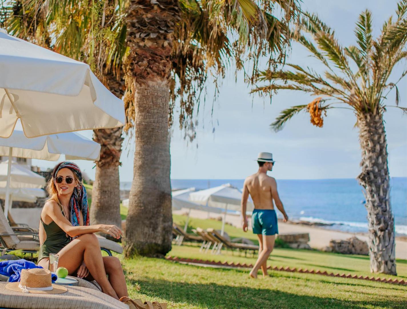 Louis Paphos Breeze zāliens ar sauļošanās krēsliem un palmām piekrastē — skats uz Vidusjūru un atpūtas zonu