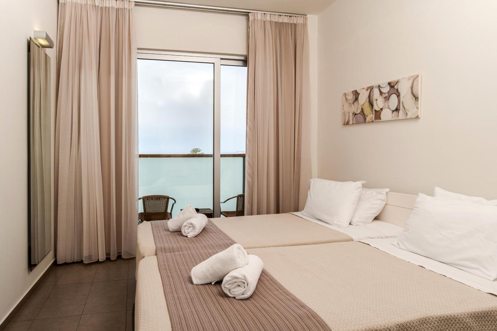 Gaišs Atlantis Boutique City Hotel numurs ar divām gultām, balkonu un pasteļtoņu aizkariem — minimālistisks un mājīgs interjers.