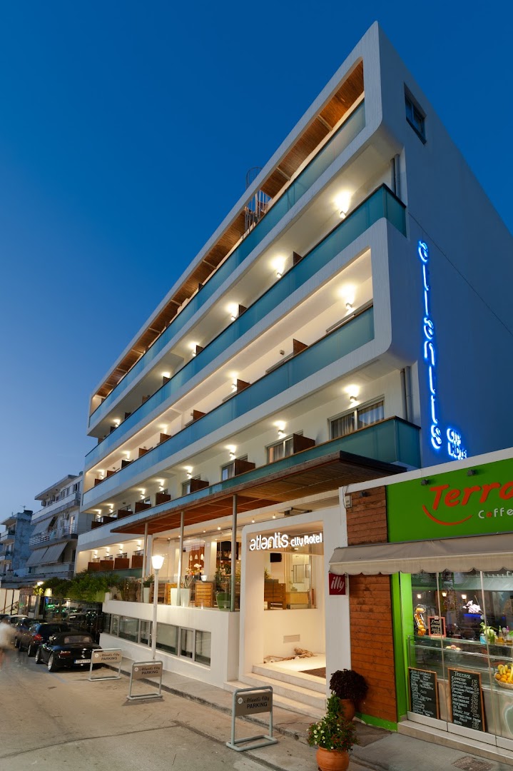 Atlantis Boutique City Hotel modernā fasāde vakarā Rodas pilsētā — izgaismoti balkoni, ieeja un viesnīcas nosaukums zilā neona gaismā.