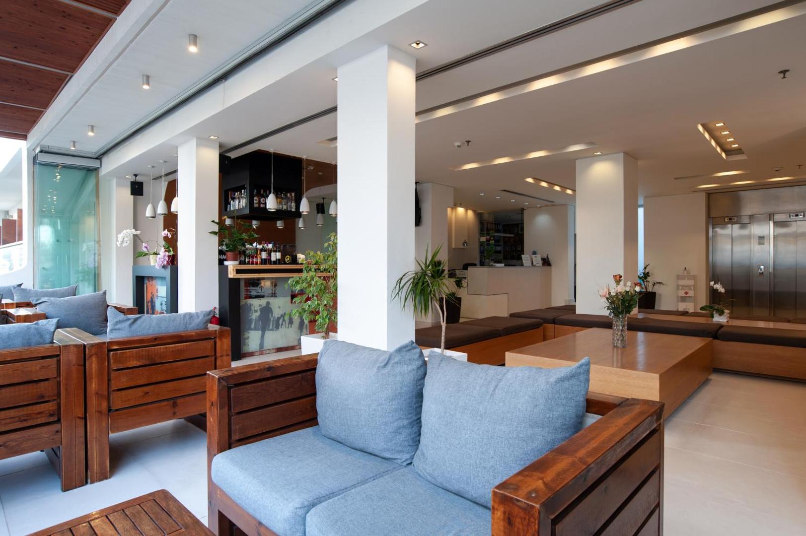 Atlantis Boutique City Hotel atpūtas zona ar koka dīvāniem un ziliem spilveniem, lobby bārs un recepcija Rodas pilsētā.