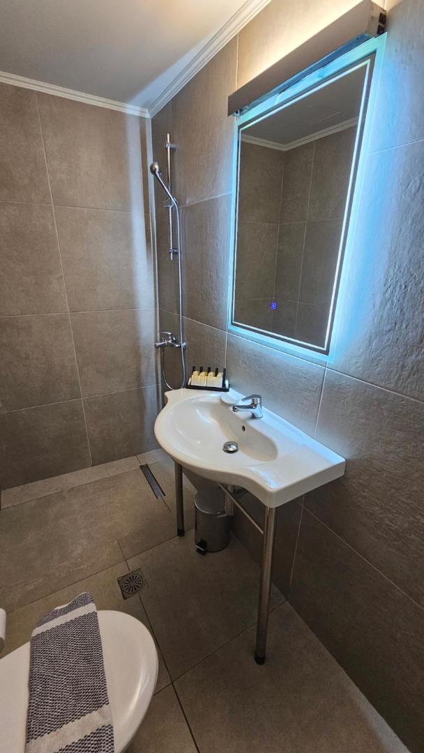 Atlantis Boutique City Hotel numura vannas istaba ar modernu izlietni, dušu un izgaismotu spoguli pelēkos toņos