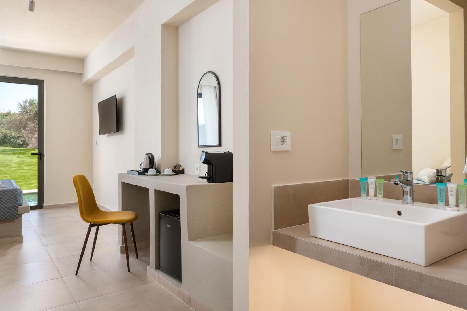Skats uz Olive Garden Hotel numura darba zonu un vannasistabas izlietni — gaišs dizains ar kafijas aparātu