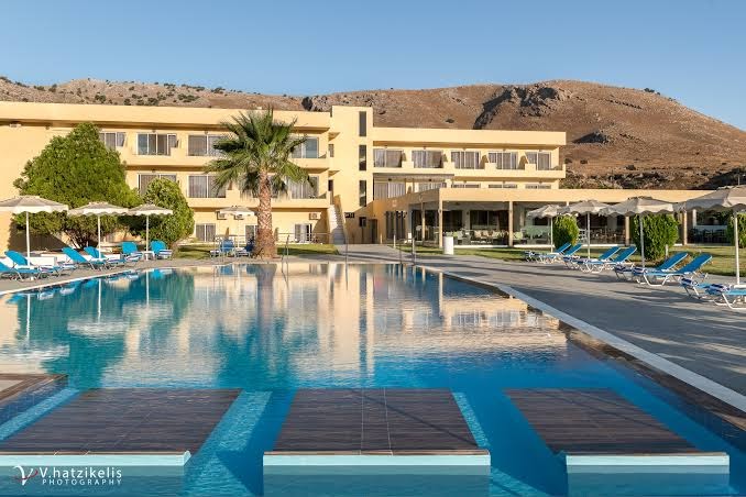 Olive Garden Hotel galvenais baseins un viesnīcas fasāde uz kalnu fona Rodā — sauļošanās terase ar moderniem krēsliem un palmām