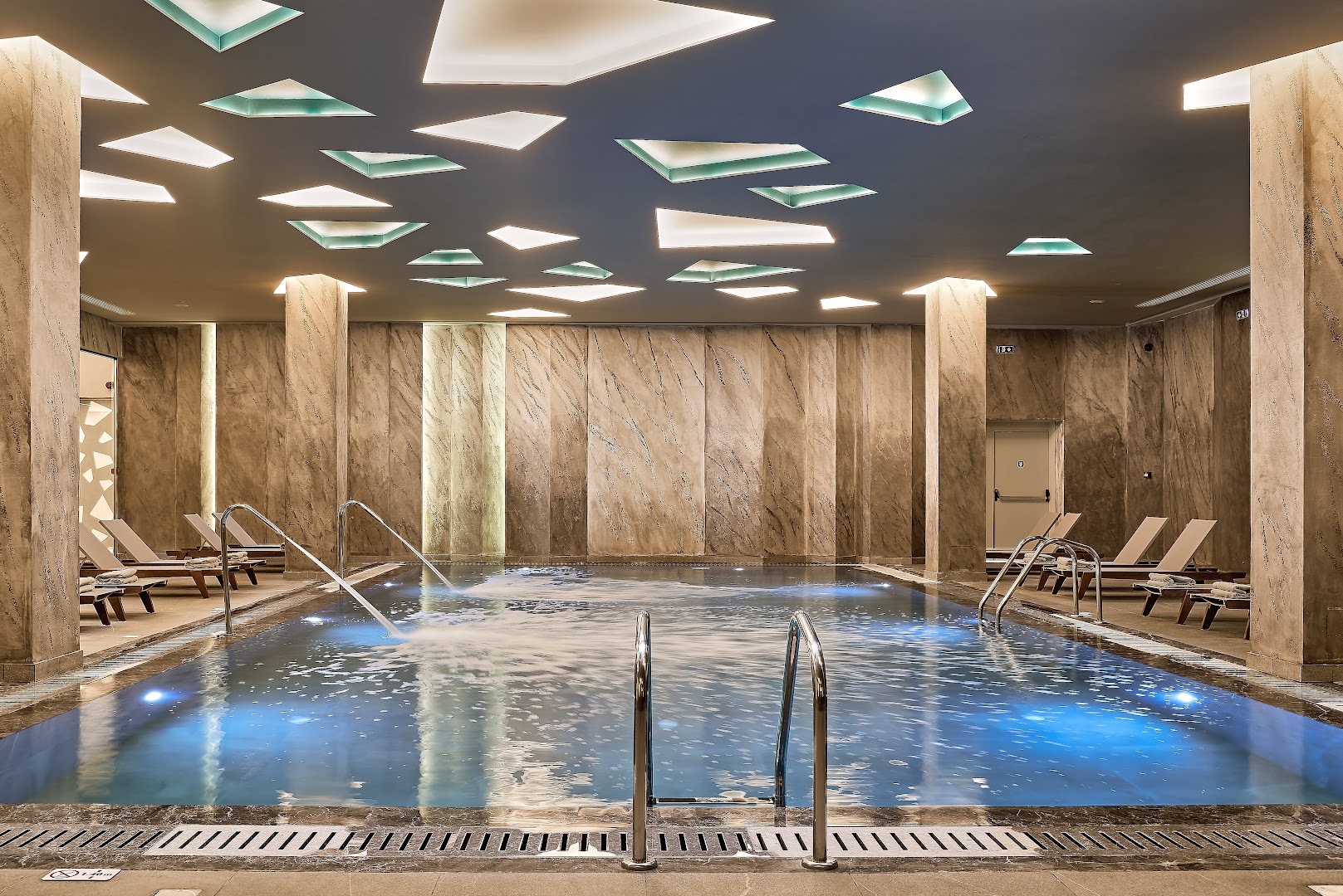 Mayia Exclusive Resort & SPA iekštelpu baseins ar masāžas strūklām, atpūtas krēsliem un modernu griestu apgaismojumu Rodas kūrortā