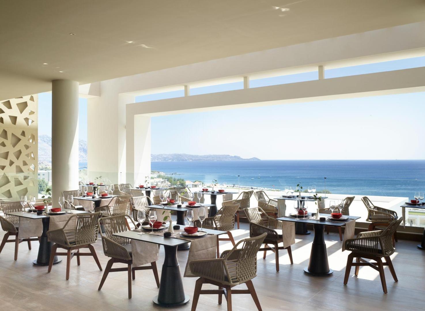 Mayia Exclusive Resort & SPA āra terases restorāns ar skatu uz Vidusjūru Rodā — eleganti klāti galdi un pīti krēsli.