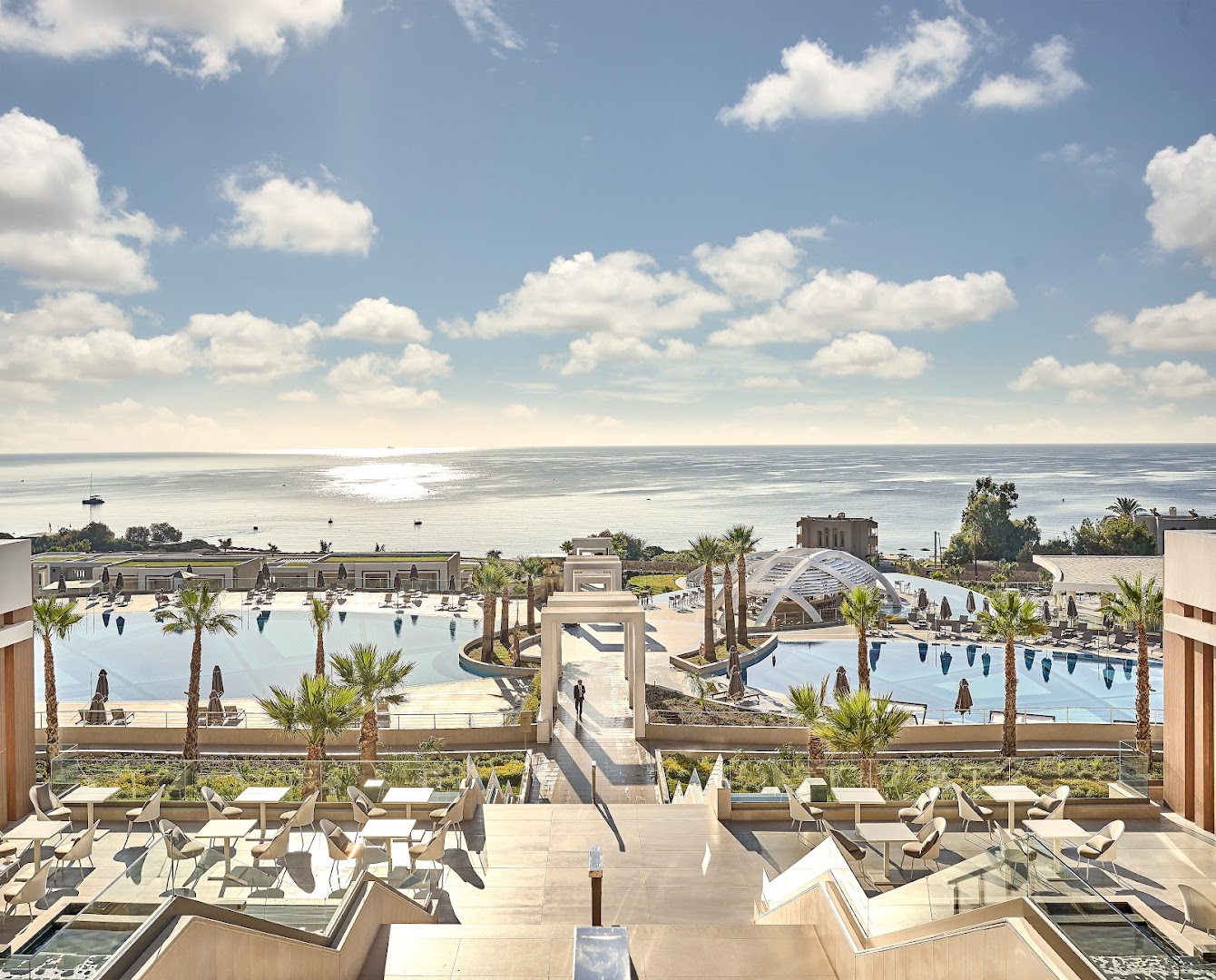Skats no Mayia Exclusive Resort & SPA terases uz Vidusjūru Rodas salā — restorāna zona ar galdiņiem un panorāmas skatu uz baseiniem