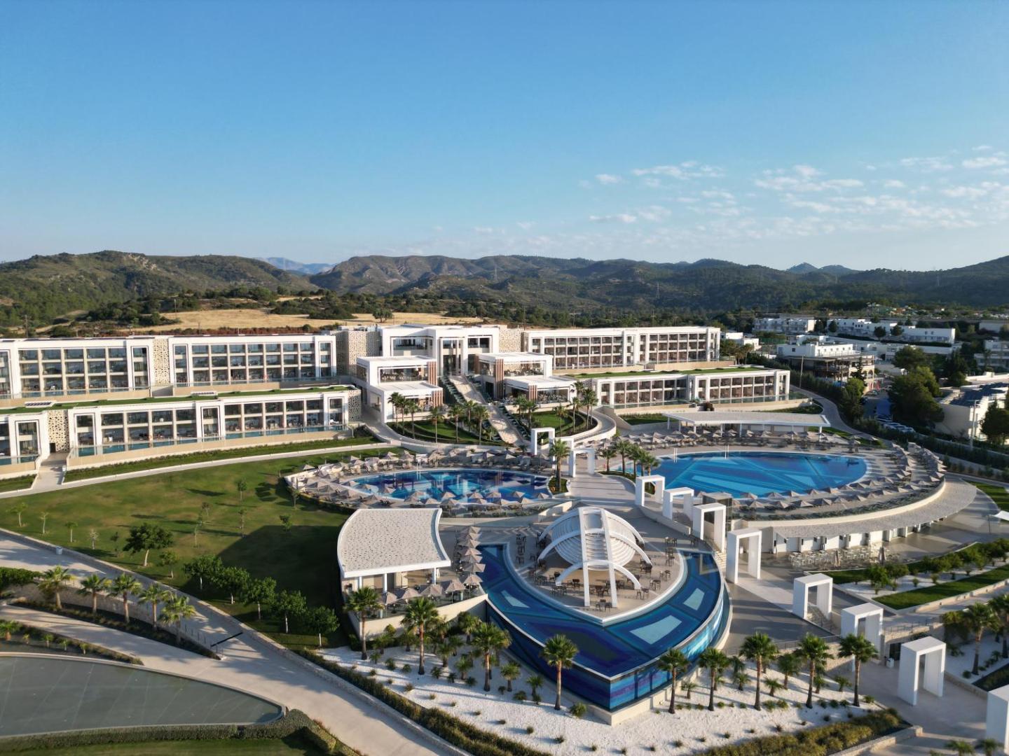 Mayia Exclusive Resort & SPA panorāmas skats no putna lidojuma Rodas salā — plaša teritorija ar vairākiem baseiniem, modernu arhitektūru un kalnu fonu
