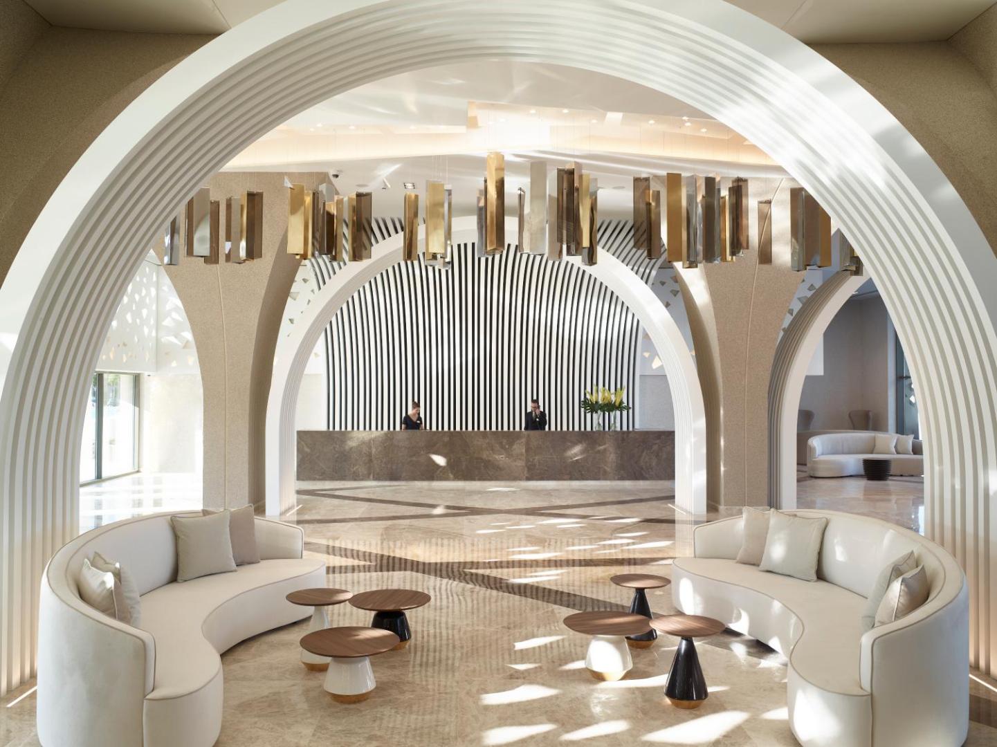 Mayia Exclusive Resort & SPA greznais lobby vestibils ar baltām arkām, dizaina dīvāniem un modernu recepcijas leti Rodas salā.