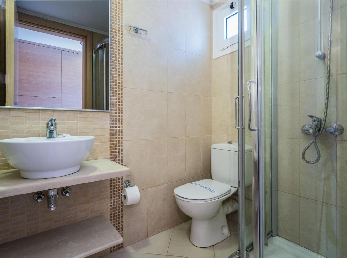 Aelius Hotel and Spa numura vannas istaba ar gaišām flīzēm, izlietni, spoguli un dušas kabīni Krētā, Grieķijā