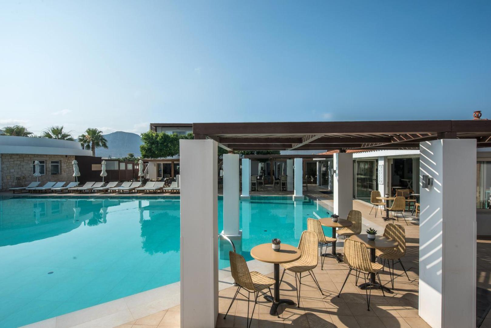 Aelius Hotel and Spa āra terase ar galdiņiem un pītiem krēsliem pie baseina, skats uz kalniem tālumā Krētā.