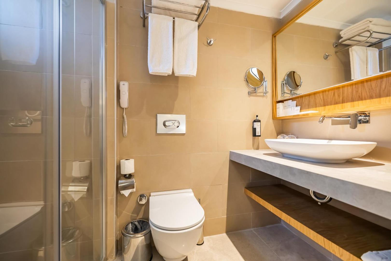 VONRESORT Golden Beach numura vannas istaba ar modernu santehniku, gaišām flīzēm, dušas kabīni un plašu spoguli koka rāmī