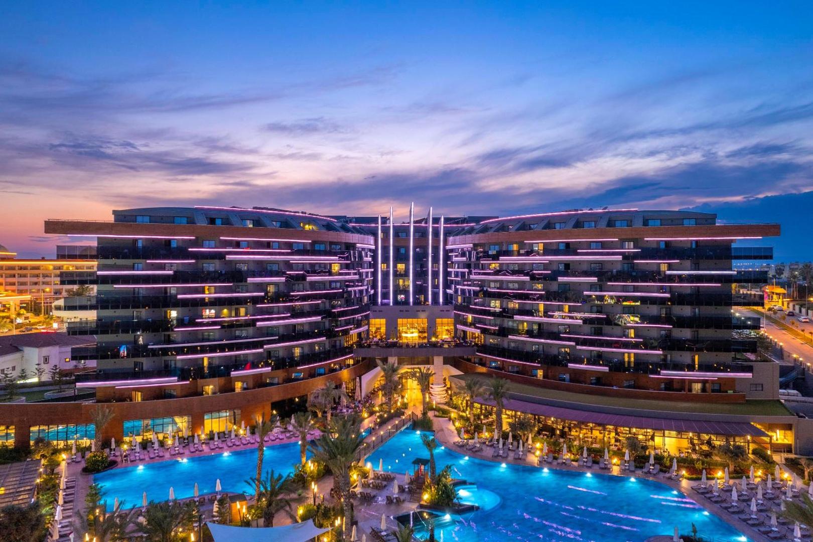 Kirman Calyptus Resort & SPA fasādes izgaismojums un baseina zona saulrieta laikā Sidē — romantiska atmosfēra un vakara gaismas