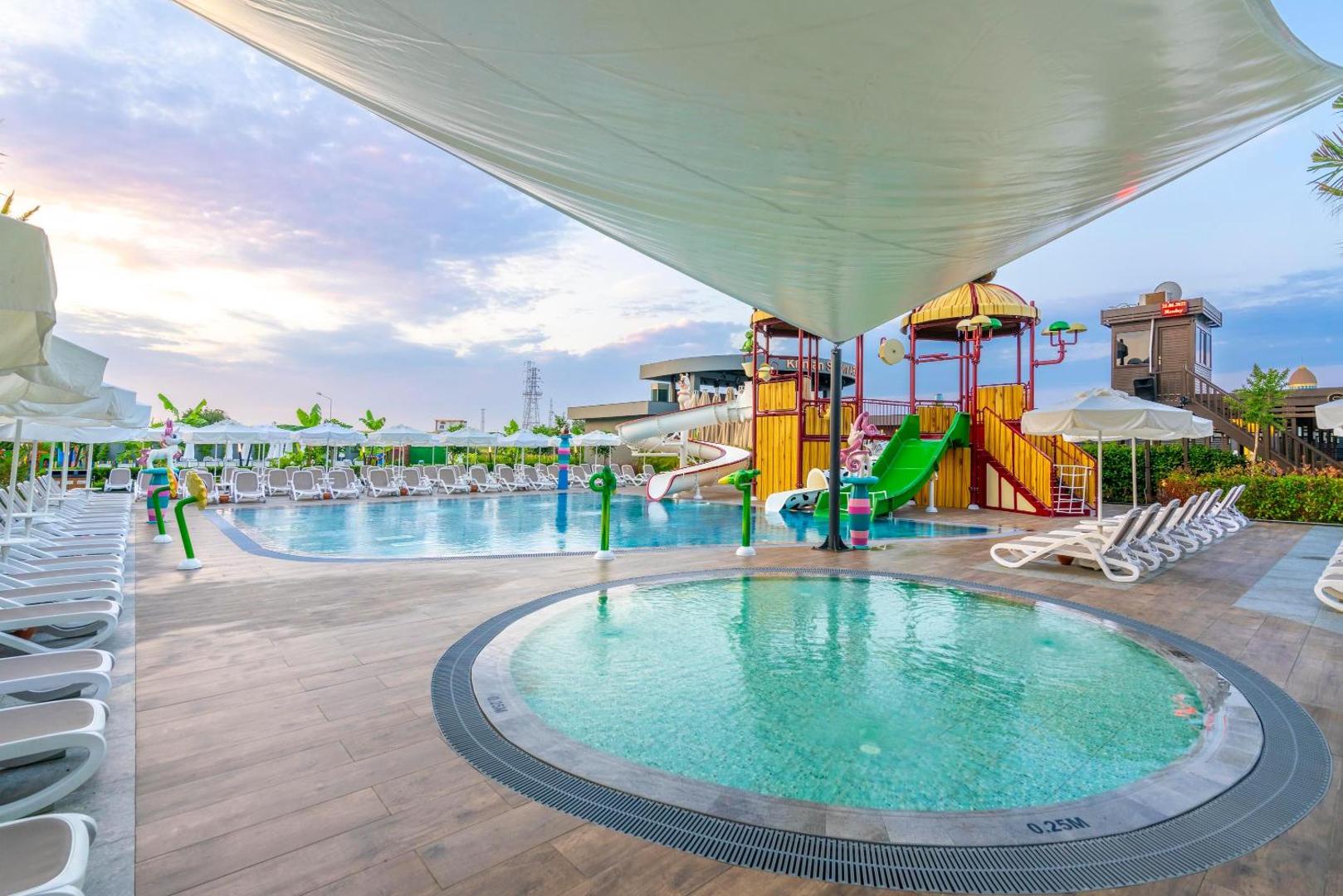Kirman Calyptus Resort & SPA āra baseins ar bērnu ūdens atrakcijām, slidkalniņiem un saulessargiem zem lielas tentu nojumes