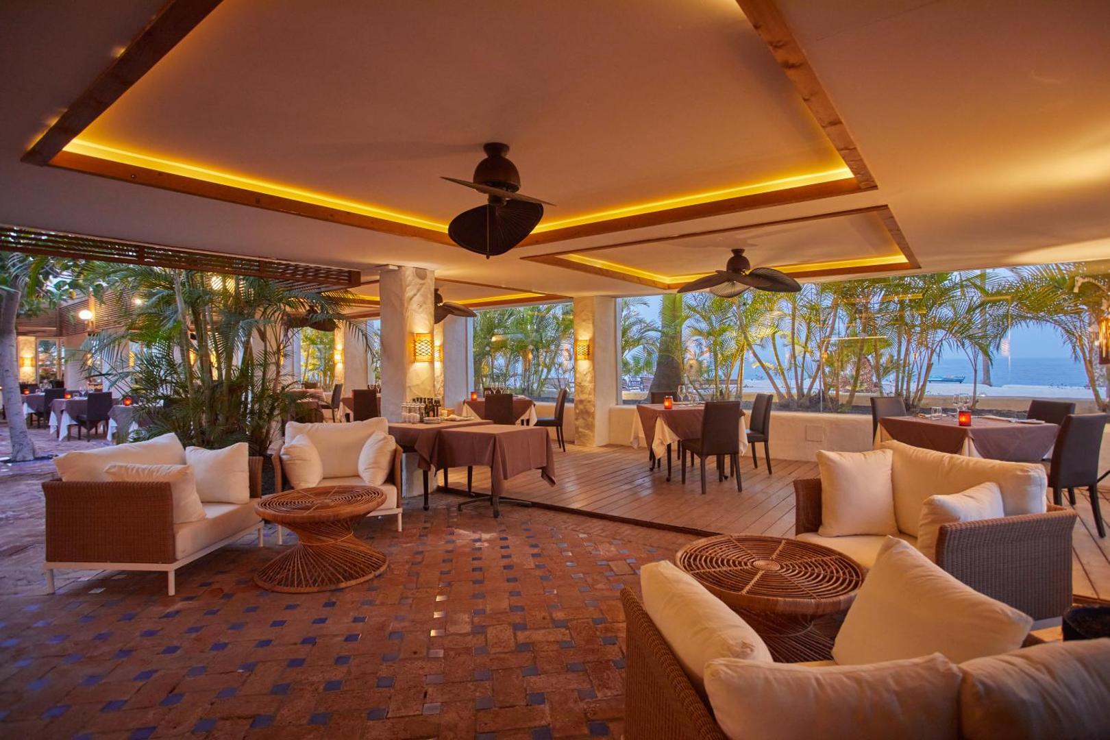 Dreams Jardin Tropical Resort & Spa restorāns ar skatu uz okeānu Tenerifē — mīkstie atpūtas krēsli un vakariņu galdi siltā apgaismojumā