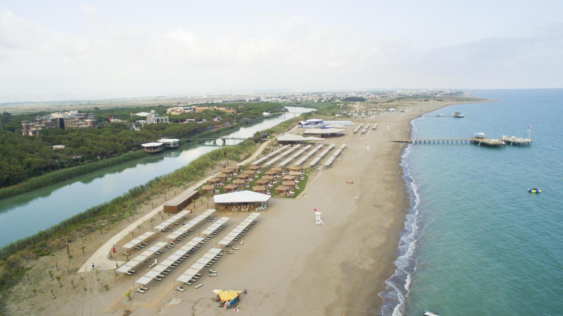 Xanadu Resort Hotel pludmales josla ar saulessargiem, zviļņiem un atpūtas namiņiem zālienā pie upes krasta Belekā