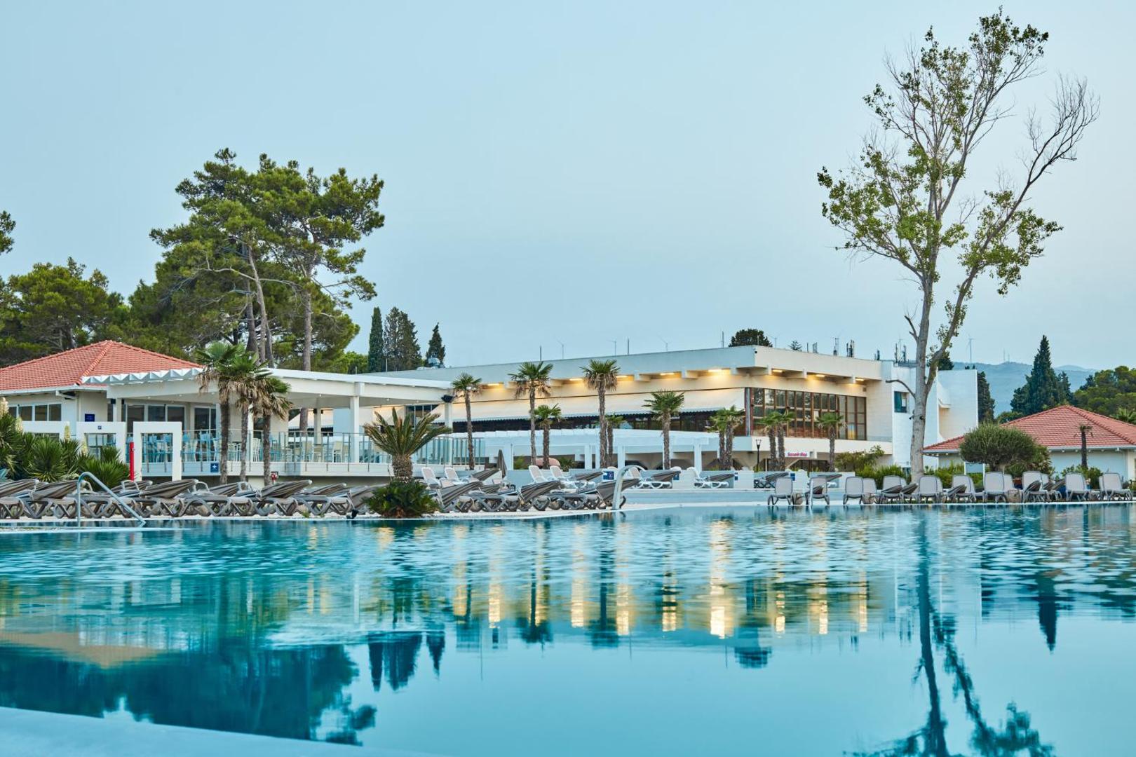 Azul Beach Resort Montenegro by Karisma galvenais baseins vakara gaismā ar skatu uz viesnīcas ēku un atpūtas krēsliem Ulciņā