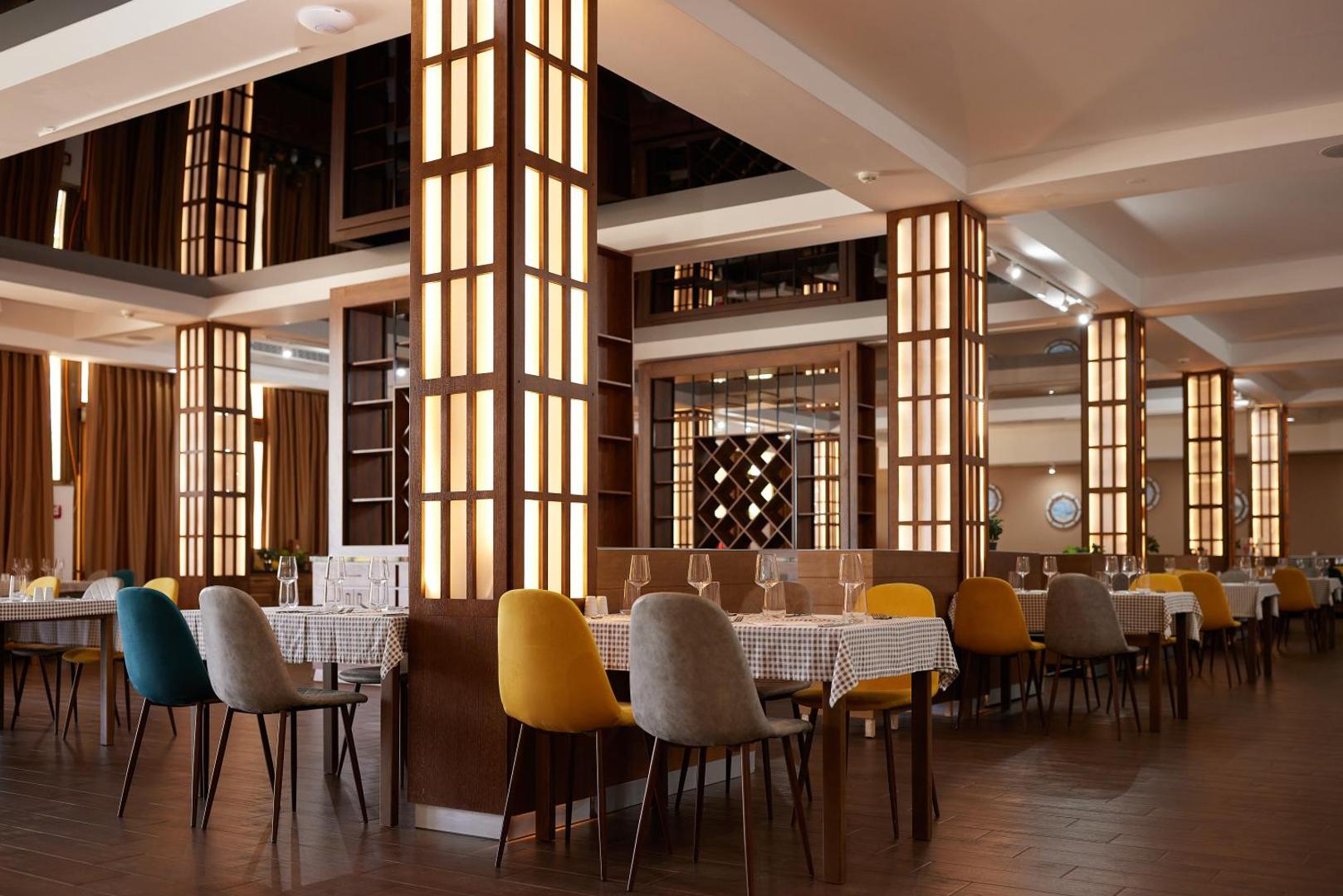 Azul Beach Resort Montenegro restorāna interjers ar modernām mēbelēm, dekoratīvām kolonnām un galdiņu servējumu vakariņām