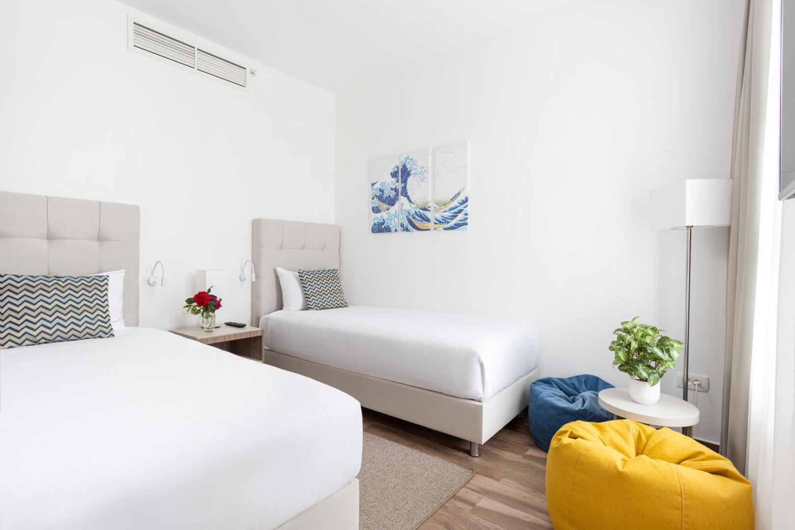 Gaišs Azul Beach Resort Montenegro viesnīcas numurs ar divām gultām, krāsainiem sēžammaisiem un modernu sienas dekoru.