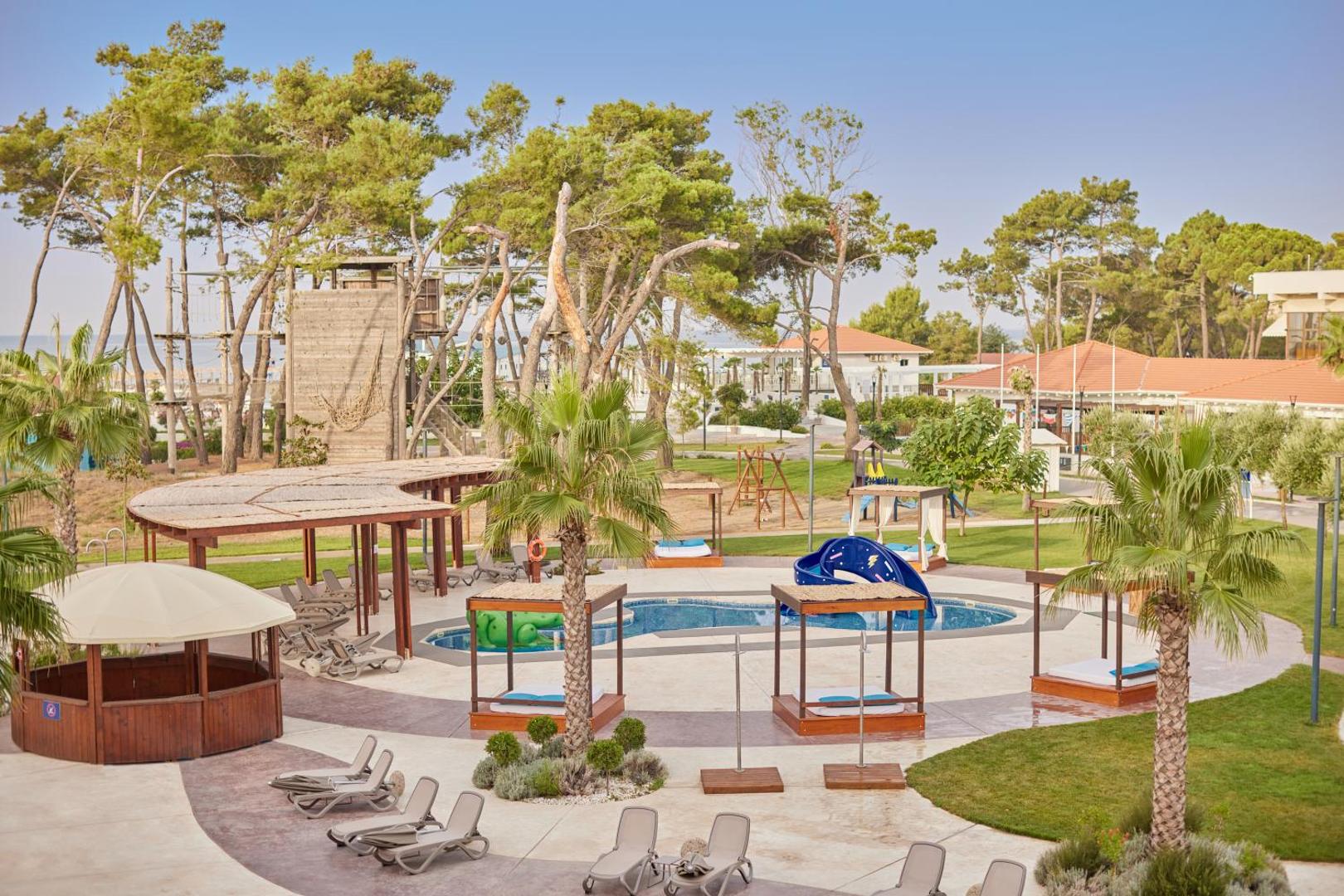 Azul Beach Resort Montenegro bērnu atpūtas zona ar seklu baseinu, nojumi un rotaļu laukumu priežu meža ielokā Ulciņā.