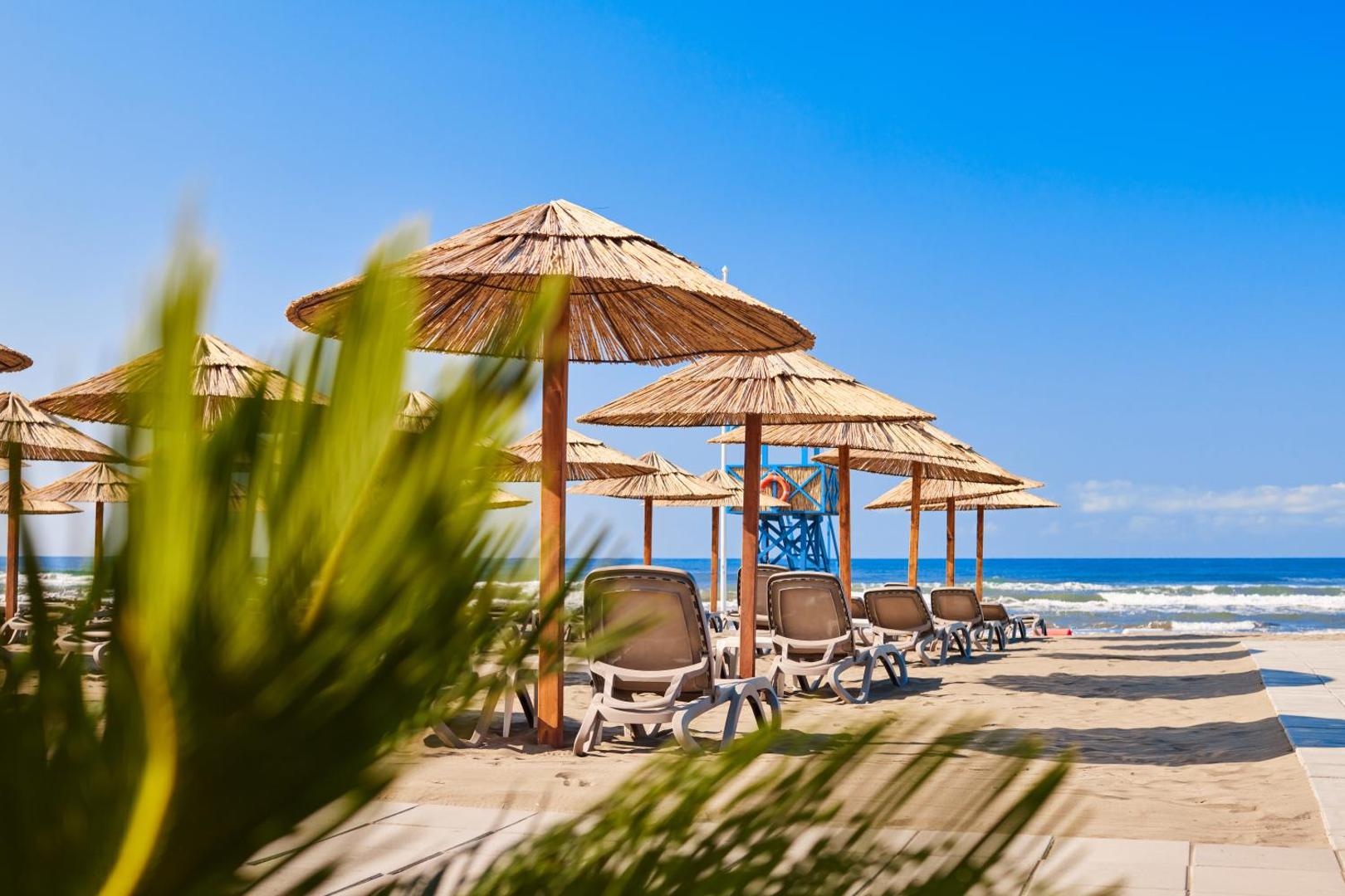 Azul Beach Resort Montenegro privātā pludmale ar salmu saulessargiem, ērtiem zviļņiem un skatu uz zilo Adrijas jūru