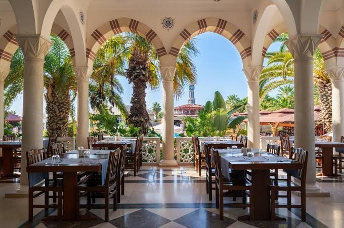 Ali Bey Club galvenais restorāns ar arkām, kolonām un koka galdiem, skats uz dārzu un palmām