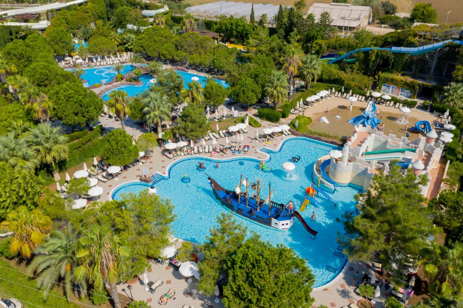 Ali Bey Club kūrorta teritorija ar vairākiem baseiniem, akvaparku un zaļojošu dārzu, skats no augšas uz atpūtas zonām.