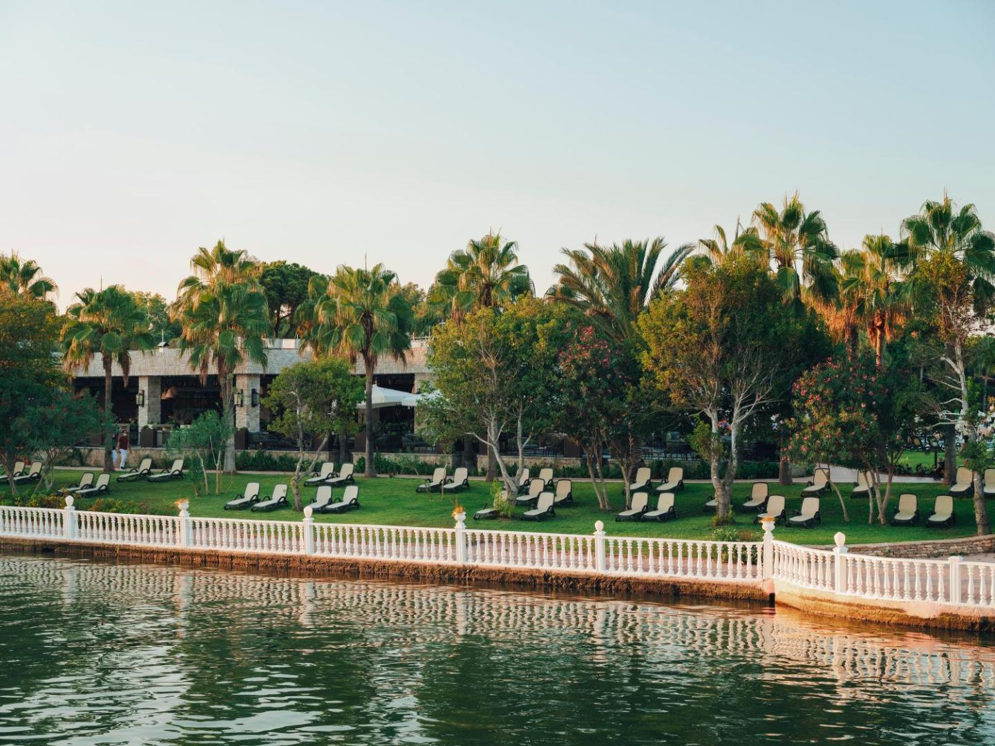 Sauļošanās krēsli zālienā zem palmām pie upes krasta Selectum Family Resort Belek kūrortā Belekā