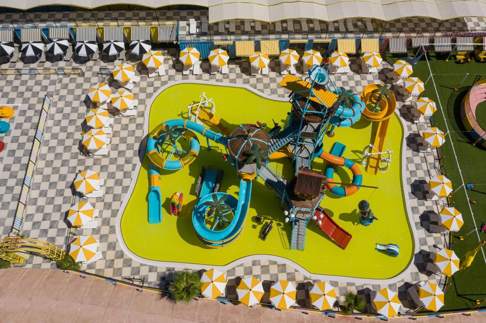 Selectum Family Resort Belek bērnu akvaparks no putna lidojuma — krāsaini slidkalniņi un sekls baseins ar dzelteniem saulessargiem Belekā