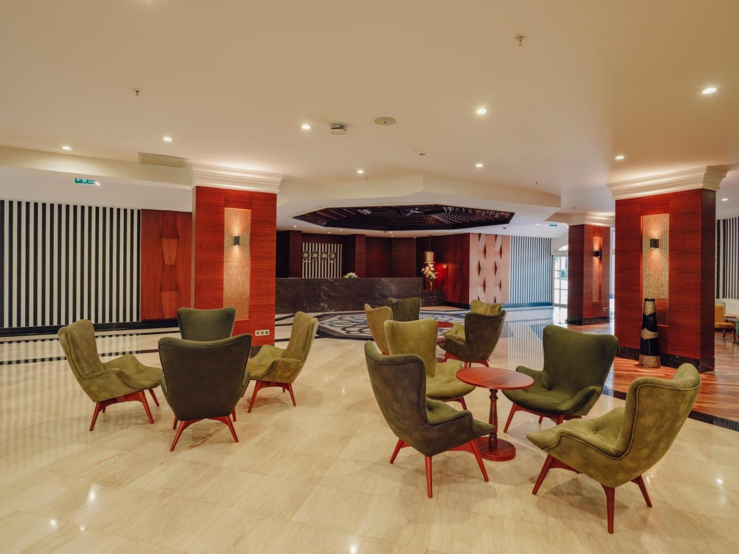 Selectum Family Resort Belek viesnīcas lobby zona ar elegantiem zaļiem atpūtas krēsliem, koka apdari un modernu apgaismojumu